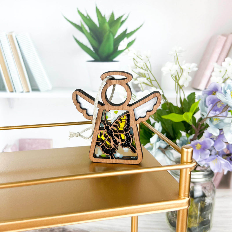 A Forged Flare® Mother's Angels® 3.5" Swallowtail Butterfly Angel Figurine sits on a gold shelf, with books, a potted plant, and flowers behind it—a vibrant display ideal for the Amazon marketplace.