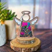 The Sweet Pea Ornament | 3.5" (H) Angel Figurine by Forged Flare® features stained-glass style wings and June’s sweet pea flowers, standing on a wood slice with potted plants softly blurred in the background.