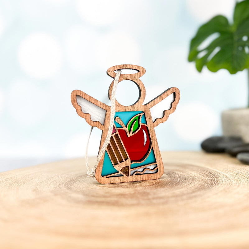 The Forged Flare® Mother's Angels® Teacher Ornament with Imperfections is a 3.5" handcrafted wooden angel figurine with wings and an apple motif, perfect as a teacher-themed centerpiece on any smooth surface.