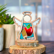 The Forged Flare® Mother's Angels® 3.5" Teacher Ornament with Imperfections features a handcrafted wooden angel with white wings, apple, pencil, and paper details—perfect as a teacher-themed centerpiece or collectible figurine.