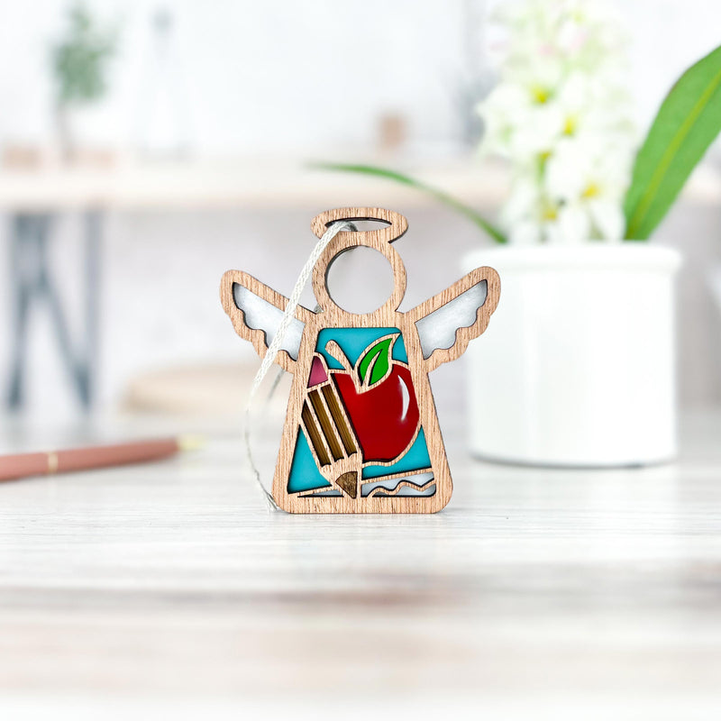Handcrafted by Forged Flare®, this 3.5" Teacher Ornament with Imperfections is a Mother's Angels® angel figurine featuring stained-glass details—a red apple and two pencils—making it a charming teacher-themed centerpiece for any space.