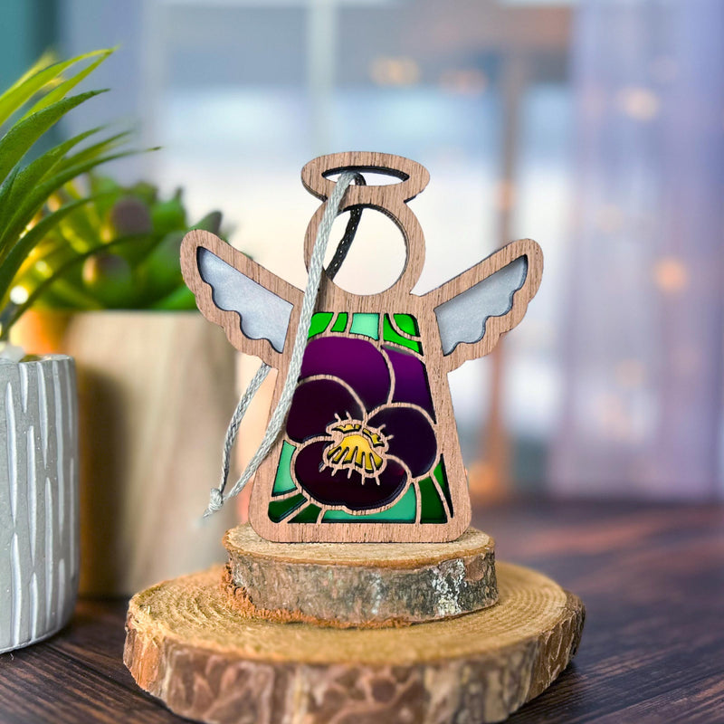 The Forged Flare® Mother's Angels® Violet Ornament with Imperfections is a 3.5" tall wooden angel figurine with painted wings, a purple flower design, and a round base—a charming collectible for any setting.