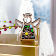 The Forged Flare® Water Lily Ornament is a 3.5" Mother's Angels® angel figurine with a stained glass-style water lily design, hanging by a white string against golden and festive holiday decor.