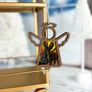 The Forged Flare® Autumn Deer Ornament, a 3.5" Mother's Angels® wooden angel figurine with reindeer and sky cutouts, hangs on a golden shelf—perfect as an autumn decor piece or unique gift for deer lovers in a snowy scene.