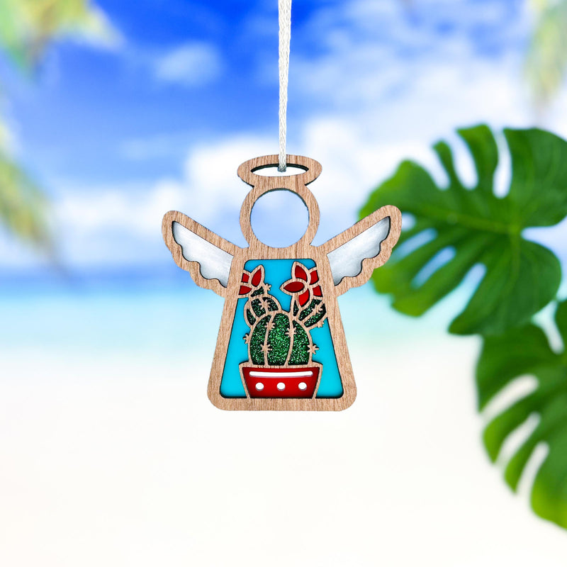 The Forged Flare® Mother's Angels® 3.5" Desert Cactus Ornament is a wooden angel figurine with wings, halo, a colorful cactus and red flowers, perfect for Southwest decor—shown against a tropical beach backdrop.