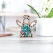 The Forged Flare® Paw Print Ornament with Imperfections is a 3.5" wooden Mother's Angels® figurine featuring a heart and paw print—a touching pet memorial gift. It stands on a light surface with blurred greenery in the background.