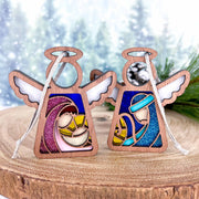 Forged Flare® Mother's Angels® Christmas Nativity 2-piece bundle features 3.5" wooden angel figurines of Mary, Joseph, and baby Jesus in stained glass-style designs, displayed against a snowy forest backdrop.