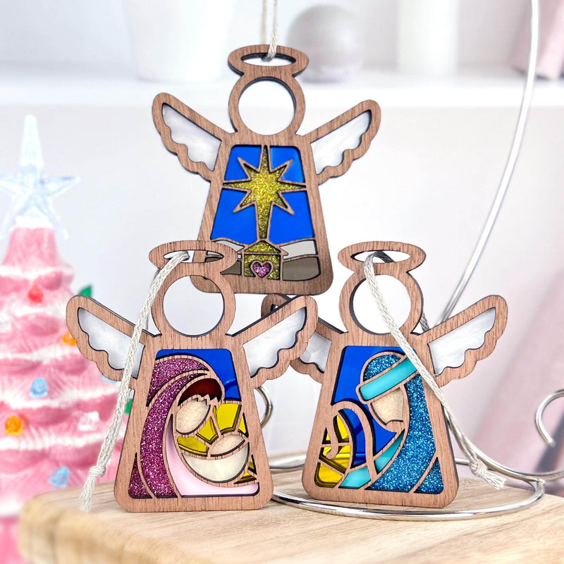 The Forged Flare® Christmas Nativity 3-Piece Bundle includes 3.5" Mother's Angels® star, Mary, and Joseph figurines with stained glass-style designs; a glowing pink Christmas tree shines in the background.