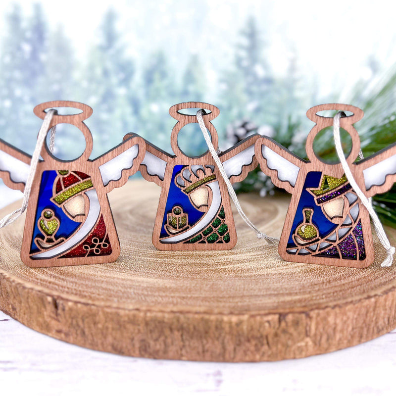 The Forged Flare® Christmas Nativity 3-Piece Bundle features Mother's Angels® 3.5" (H) angel figurines representing the Three Wise Men, displayed on a round wooden stand, evoking a charming and peaceful holiday scene.