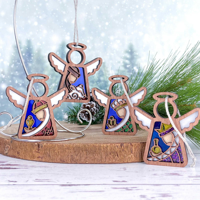 The Forged Flare® Christmas Nativity 4-Piece Bundle features 3.5" Mother's Angels® figurines of the Three Wise Men and Shepherd, each with colorful stained-glass insets, displayed against snowy pine branches on a wooden slab.