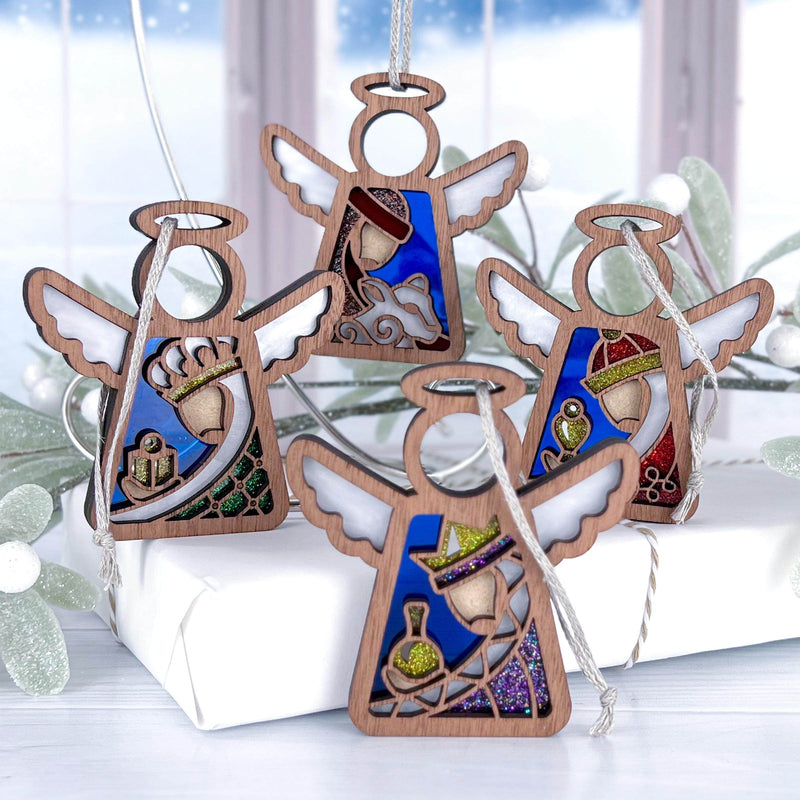 The Forged Flare® Christmas Nativity 4-Piece Bundle features 3.5" Mother's Angels® figurines of the Three Wise Men and a Shepherd, each with stained glass-style accents, displayed with a snowy window and festive white gift.