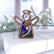 The Forged Flare® Christmas Nativity Green Wise Man 3.5" Angel Figurine rests on a twine-wrapped white gift, surrounded by frosted greenery with a window in the background, capturing a festive holiday scene.