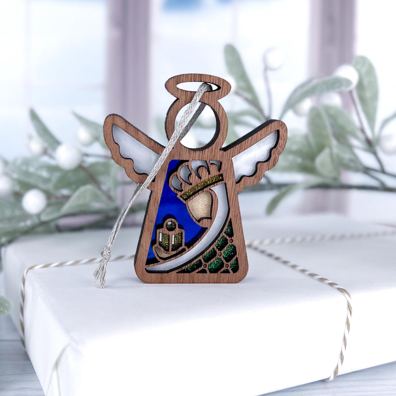 The Forged Flare® Christmas Nativity Green Wise Man 3.5" Angel Figurine rests on a twine-wrapped white gift, surrounded by frosted greenery with a window in the background, capturing a festive holiday scene.