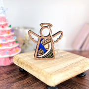 The Forged Flare® Mother's Angels® Christmas Nativity Green Wise Man angel figurine, 3.5" tall, stands on a small board with vivid details. Behind it is a pink, tree-shaped decoration with colorful lights—perfect for holiday displays.