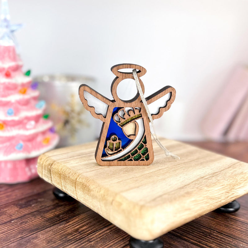 The Forged Flare® Mother's Angels® Christmas Nativity Green Wise Man angel figurine, 3.5" tall, stands on a small board with vivid details. Behind it is a pink, tree-shaped decoration with colorful lights—perfect for holiday displays.