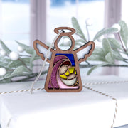 The Forged Flare® Mother's Angels® 3.5" Christmas Nativity Mary Mother of Jesus angel figurine sits atop a white gift box, creating a charming festive gift with holiday greenery and a snowy window blurred in the background.