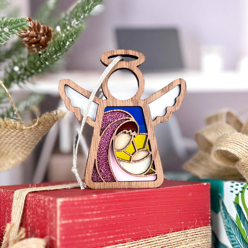 The Forged Flare® Christmas Nativity Mary Mother of Jesus 3.5" Angel Figurine sits atop wrapped gifts, with pine branches and ribbon enhancing the festive scene in the background.