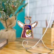 The Forged Flare® Christmas Nativity Mary Mother of Jesus 3.5" Angel Figurine, part of Mother's Angels®, features elegant white wings and stained glass details—perfect as a festive gift or decor accent. A blurred plant and books rest in the background on wood.