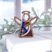 The Forged Flare® Christmas Nativity Red Wise Man 3.5" Mother's Angels® figurine stands on a white gift box with a snowy window and frosted greenery in the background, featuring painted wings, halo, and colorful details.