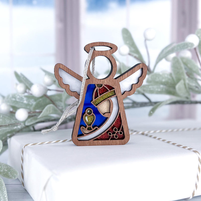 The Forged Flare® Christmas Nativity Red Wise Man 3.5" Mother's Angels® figurine stands on a white gift box with a snowy window and frosted greenery in the background, featuring painted wings, halo, and colorful details.