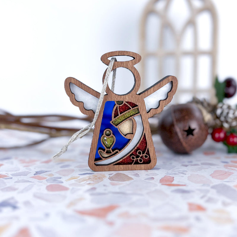 The Forged Flare® Christmas Nativity Red Wise Man 3.5" Angel Figurine from Mother's Angels® stands on terrazzo, surrounded by festive touches like a bell, berries, and window-shaped décor for a charming holiday scene.