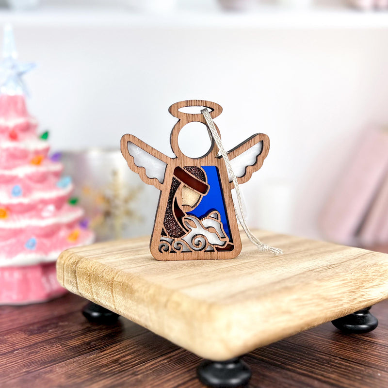 The Forged Flare® Mother's Angels® Christmas Nativity Shepherd With Sheep 3.5" angel figurine is displayed on a small riser before a pink Christmas tree, perfect as a Nativity ornament or holiday gift.