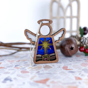 The Forged Flare® Mother's Angels® 3.5" Christmas Nativity Star Angel Figurine, featuring white wings and a blue-gold star design with imperfections, hangs on a patterned surface—an ideal meaningful holiday gift among festive décor.