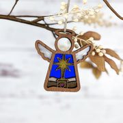 The Forged Flare® Mother's Angels® 3.5" Christmas Nativity Star Angel figurine, featuring wings, a star, and pink heart, hangs from a branch with white berries and brown leaves—an inspiring holiday gift with beautiful imperfections.