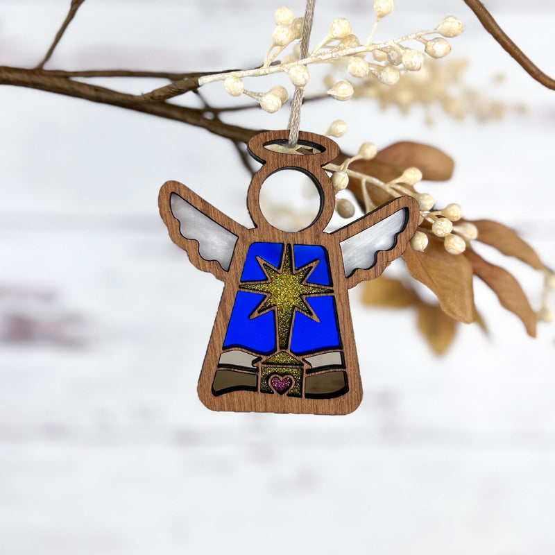 The Forged Flare® Mother's Angels® 3.5" Christmas Nativity Star Angel figurine, featuring wings, a star, and pink heart, hangs from a branch with white berries and brown leaves—an inspiring holiday gift with beautiful imperfections.