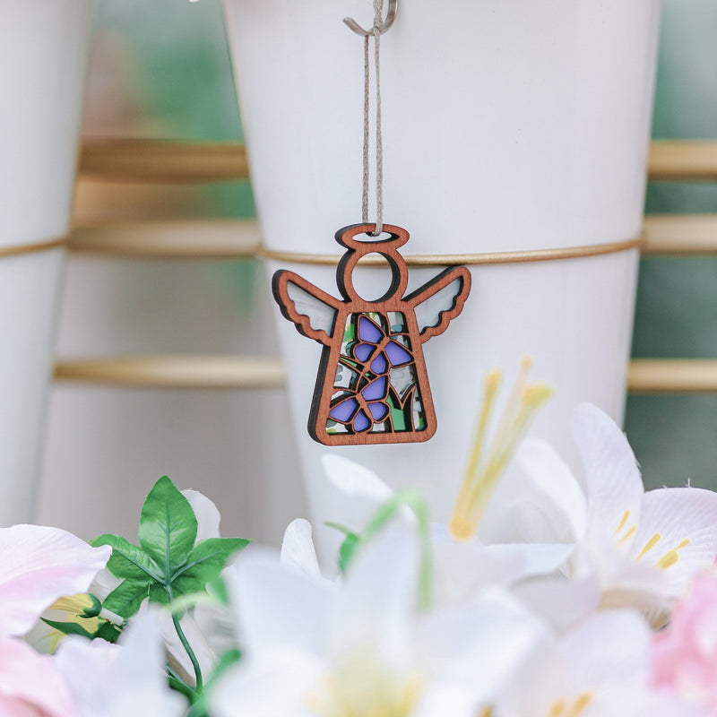 A Forged Flare® Warehouse Return - Playful Purple Butterflies Ornament (3.5" H) Mother's Angels® figurine adds charm with stained glass wings—an eye-catching find among white vases, lilies, and lush green leaves for any Amazon shopper.