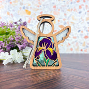 The Iris Ornament | 3.5" (H) Angel Figurine from Forged Flare®’s Mother's Angels® features stained glass-style wings and a purple iris, perfect for collections or unique flower decor. Displayed with white and purple flowers in the background.