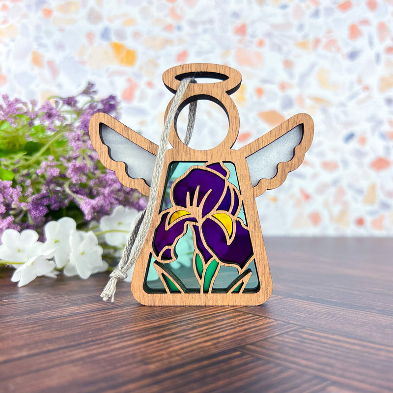 The Iris Ornament | 3.5" (H) Angel Figurine from Forged Flare®’s Mother's Angels® features stained glass-style wings and a purple iris, perfect for collections or unique flower decor. Displayed with white and purple flowers in the background.