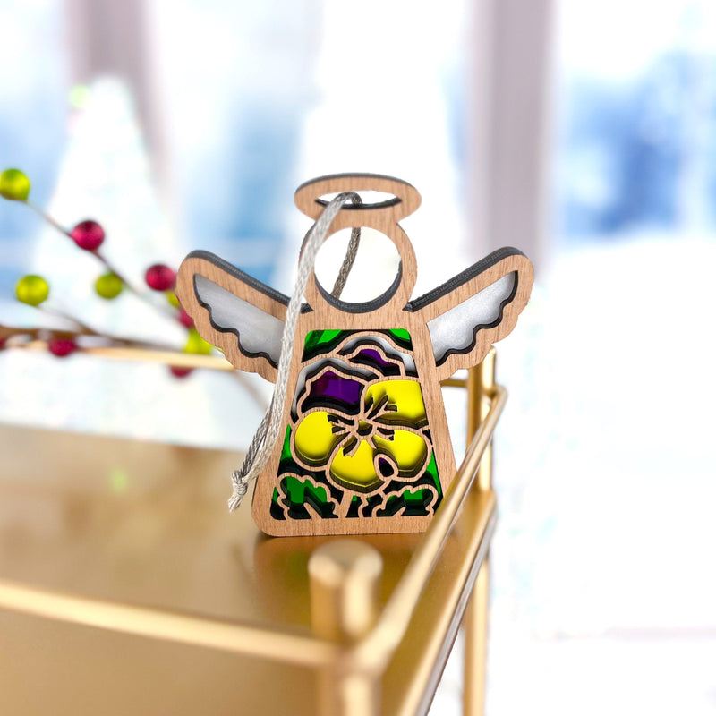 The Forged Flare® Pansy Ornament is a 3.5" (H) Mother's Angels® figurine with stained glass-style yellow and purple pansies, hanging from a white string—perfect for angel collections or as a Christmas tree ornament.
