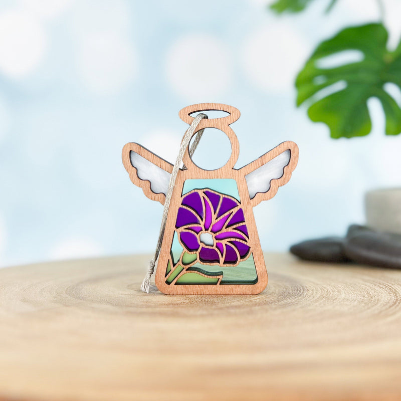 The Forged Flare® Purple Morning Glory Ornament, a 3.5" Mother's Angels® wooden angel figurine with white wings and a stained-glass style September birth flower, stands on a light wood surface with a blurred plant in the background.