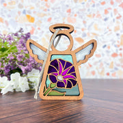The Forged Flare® Purple Morning Glory Ornament | 3.5" (H) Mother's Angels® figurine features white wings and a hand-painted purple morning glory birth flower, displayed on wood surrounded by purple and white blooms, with a colorful mosaic background.