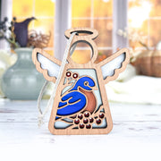 The Forged Flare® Bluebird Ornament—a 3.5" Mother's Angels® wooden angel figurine with white wings and a blue and brown bird—makes a thoughtful Memorial Gift, shown on a light surface with blurred vases and window in the background.