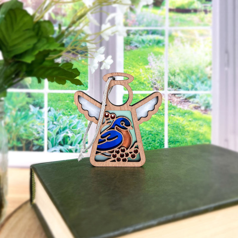 The Bluebird Ornament | 3.5" (H) Angel Figurine by Forged Flare® from Mother's Angels® rests on a green book, featuring a painted bluebird and flowers—a charming bird lover gift with garden vibes.