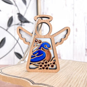 The Forged Flare® Bluebird Ornament | 3.5" (H) Mother's Angels® features a blue and orange bird design on wood—ideal as a Memorial or Bird Lover Gift. Displayed on light wood with blurred bird branch metal wall art in the background.
