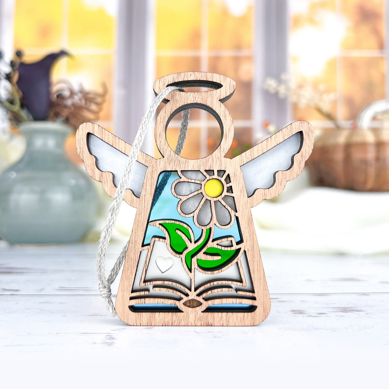 The Forged Flare® Book Lovers Ornament, a 3.5" Mother's Angels® figurine with wings, cutout book, heart, green leaves, yellow flower, and blue stained glass—an ideal author or book club gift.