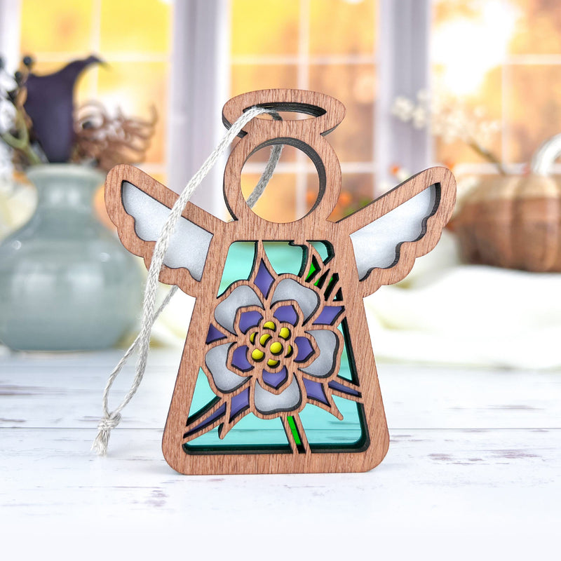 The Forged Flare® Columbine Ornament is a 3.5" Mother's Angels® wooden angel figurine with stained glass featuring a purple columbine flower and yellow center—perfect as a Christmas tree ornament or heartfelt gift.