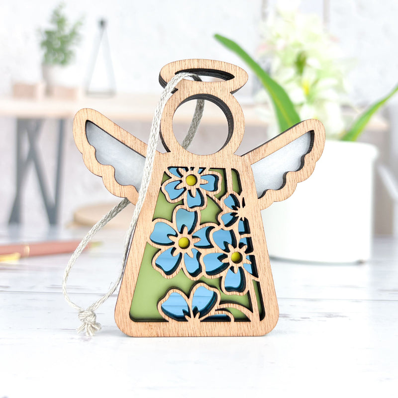 The Forged Flare® Forget-Me-Not Ornament is a 3.5" tall Mother's Angels® wooden angel figurine with cut-out blue flowers, a halo, and wings—perfect as a charming Christmas tree ornament.