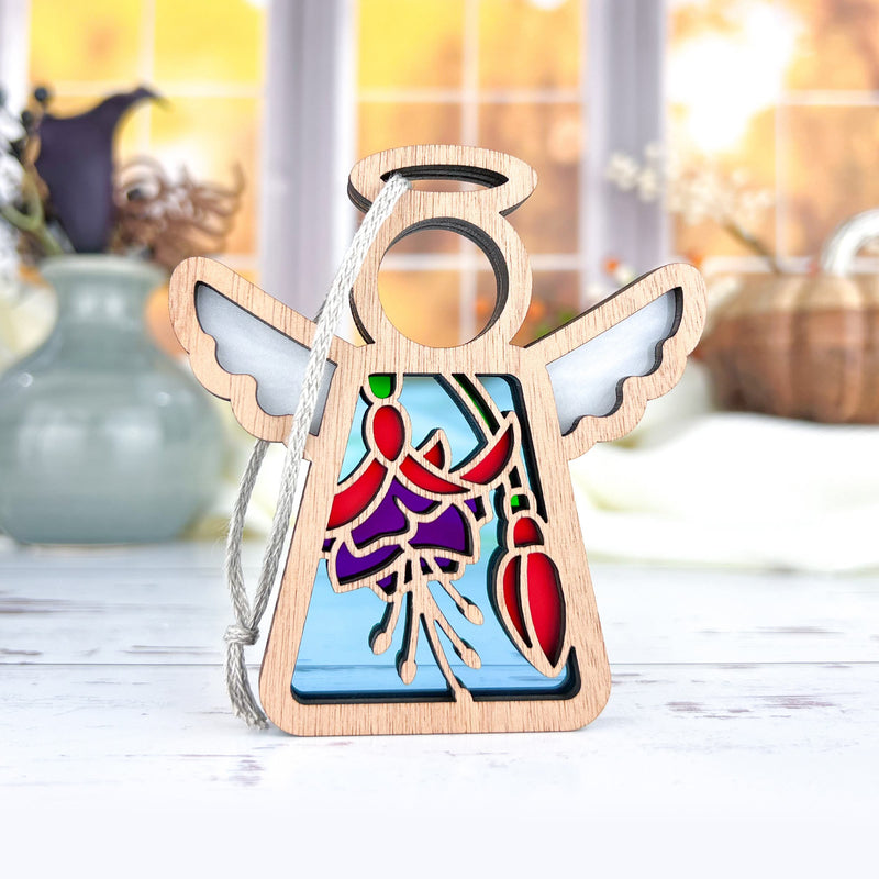 The Forged Flare® Mother's Angels® Fuchsia Ornament is a 3.5" high wooden angel figurine with white wings and a stained-glass-style fuchsia flower, suspended by a silver cord—ideal as a Christmas tree ornament or thoughtful flower gift.