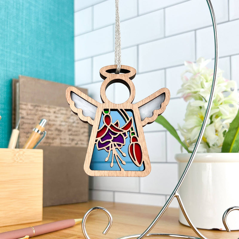 The 3.5" Fuchsia Ornament Angel Figurine by Forged Flare® Mother's Angels® features cut-out wings and a stained-glass look—ideal as a Christmas tree ornament or keepsake for any desk, surrounded by pens, notebooks, and flower gifts.