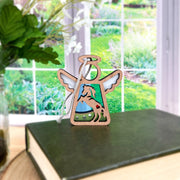 The Forged Flare® Horse Ornament | 3.5" (H) Angel Figurine from Mother's Angels® stands on a green book beside a flower vase with a garden view—ideal as unique horse decor or a heartfelt horse memorial gift.