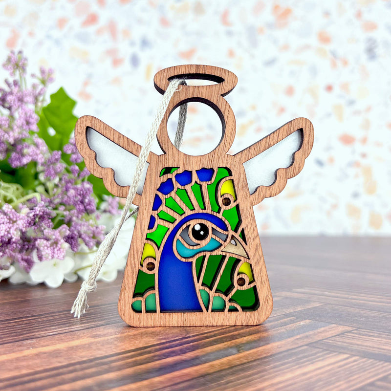The Peacock Ornament by Forged Flare® is a 3.5" Mother's Angels® angel figurine featuring stained-glass style wings and a vibrant peacock design—an ideal gift for bird lovers.