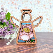 The Forged Flare® Pink Peony Ornament is a 3.5" Mother's Angels® wooden angel figurine with white wings, halo, tassel, and a stained-glass-style pink peony—perfect as a Christmas tree ornament or gift.