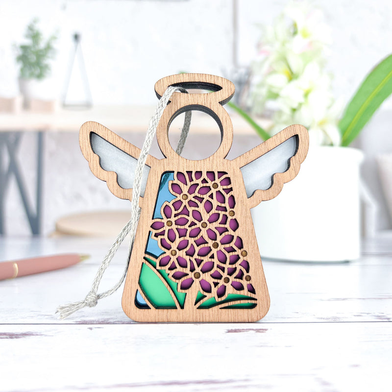 The Forged Flare® Purple Lilac Ornament is a 3.5" Mother's Angels® angel figurine with cut-out floral patterns and colorful accents, perfect as a Christmas tree ornament or decor to add a soft, cozy touch to your space.