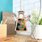 The Red-Eyed Tree Frog Ornament by Forged Flare® is a 3.5" Mother's Angels® figurine, shown hanging from a stand on a desk with a notebook, pens, and white flower vase—an ideal frog gift or unique Christmas tree ornament.