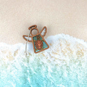 The Forged Flare® Sea Turtle Ornament, a 3.5" Mother's Angels® wooden angel figurine with a turtle design, rests on sandy beach waves—an enchanting accent for any coastal or beach house decor.