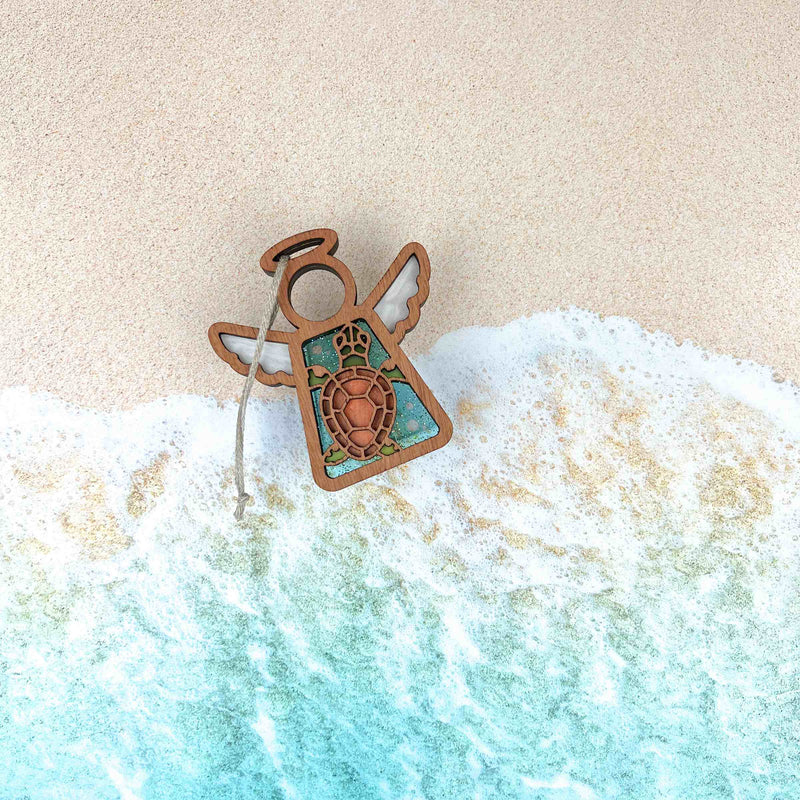 The Forged Flare® Sea Turtle Ornament, a 3.5" Mother's Angels® wooden angel figurine with a turtle design, rests on sandy beach waves—an enchanting accent for any coastal or beach house decor.
